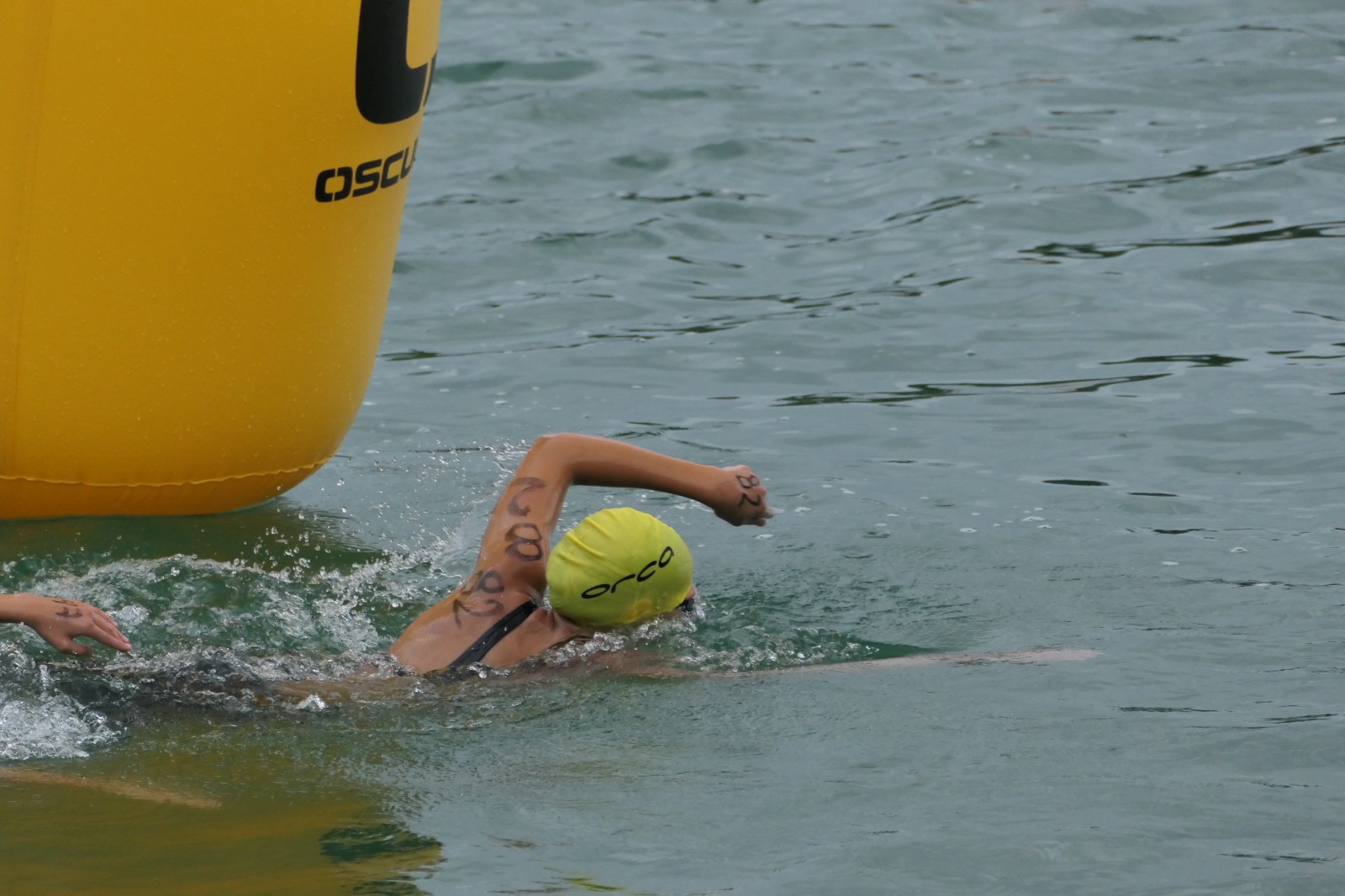 Schwimmer mit gelber Badekappe beim Freiwasserschwimmen neben gelber Boje