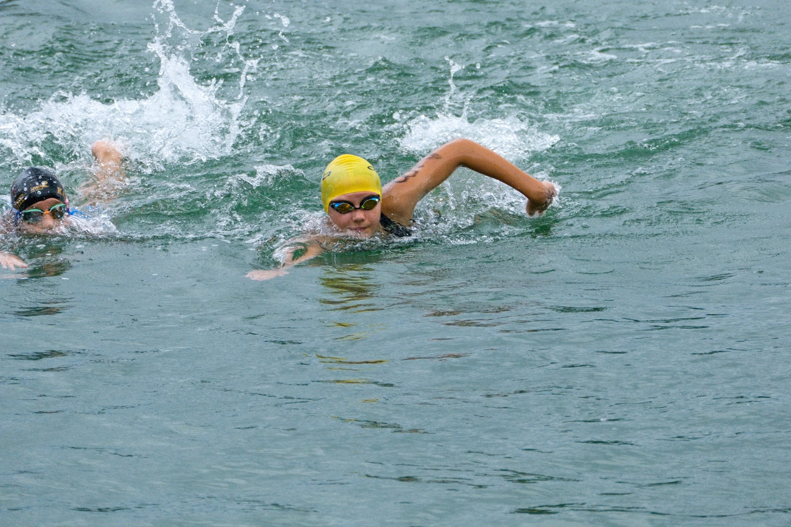 Kind schwimmt mit gelber Badekappe im Freiwasser bei einem Wettkampf