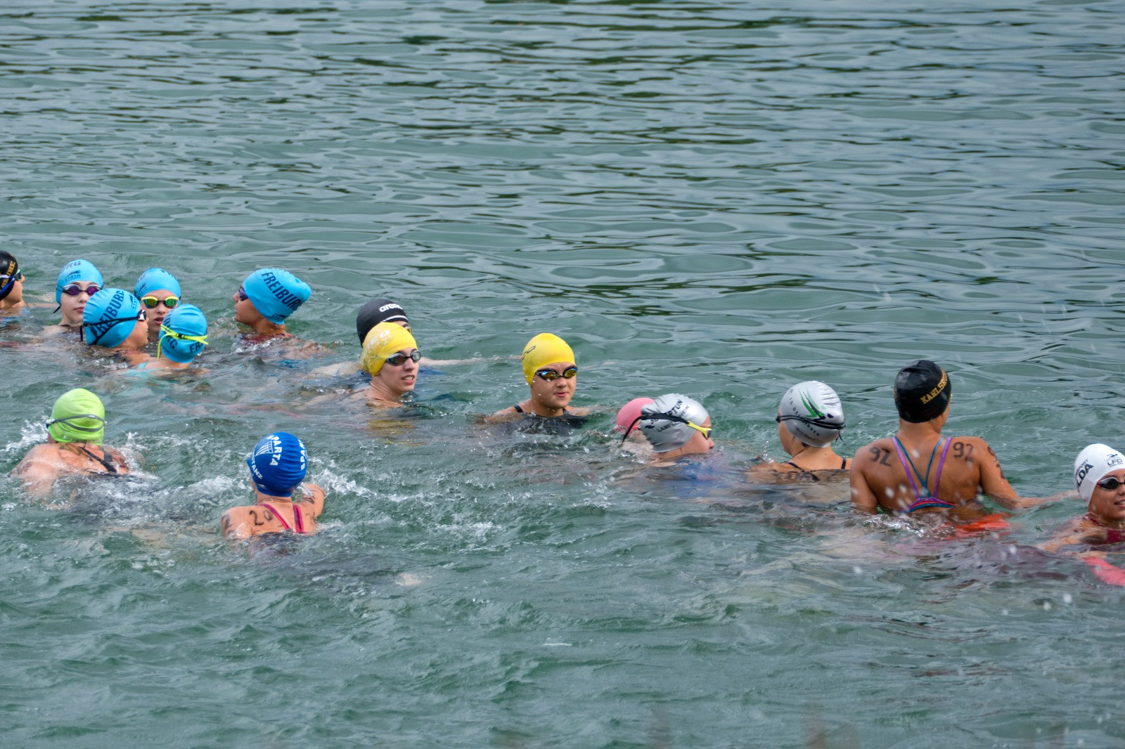 Gruppe von Schwimmerinnen mit Badekappen bei einem Freiwasserwettkampf