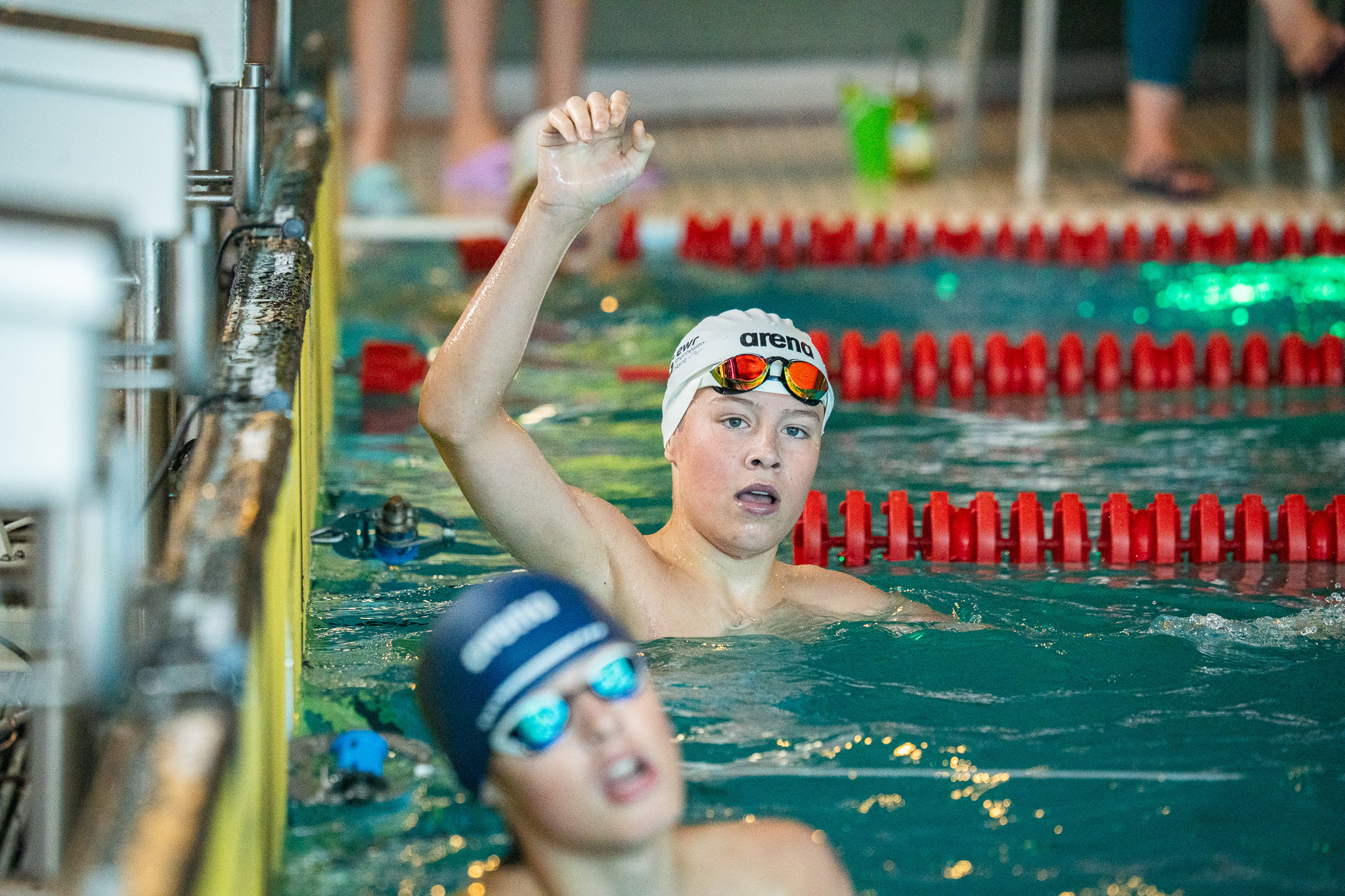 Schwimmer im Hallenbad hebt die Hand nach dem Wettkampf, Schwimmwettbewerb mit Arena-Schwimmkappen