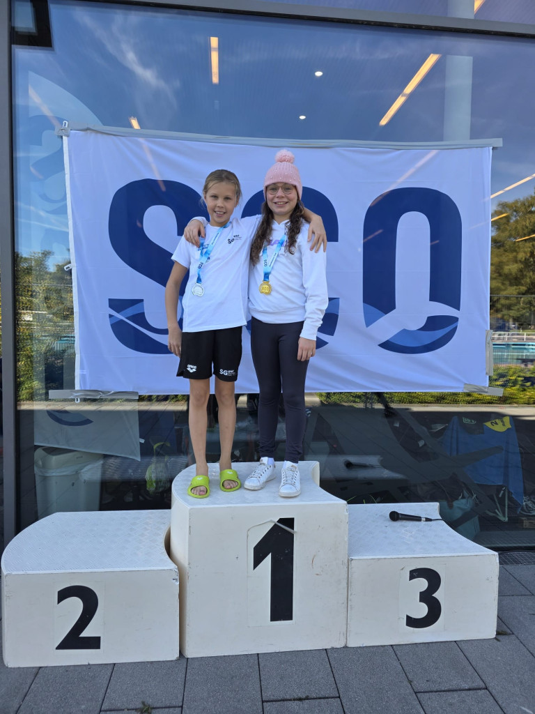 Zwei junge Schwimmerinnen mit Medaillen auf dem Siegerpodest vor einem SCO-Banner
