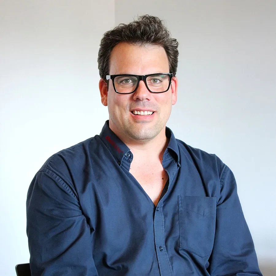 Christo Costerus sitzt in einem dunkelblauen Hemd vor hellem Hintergrund