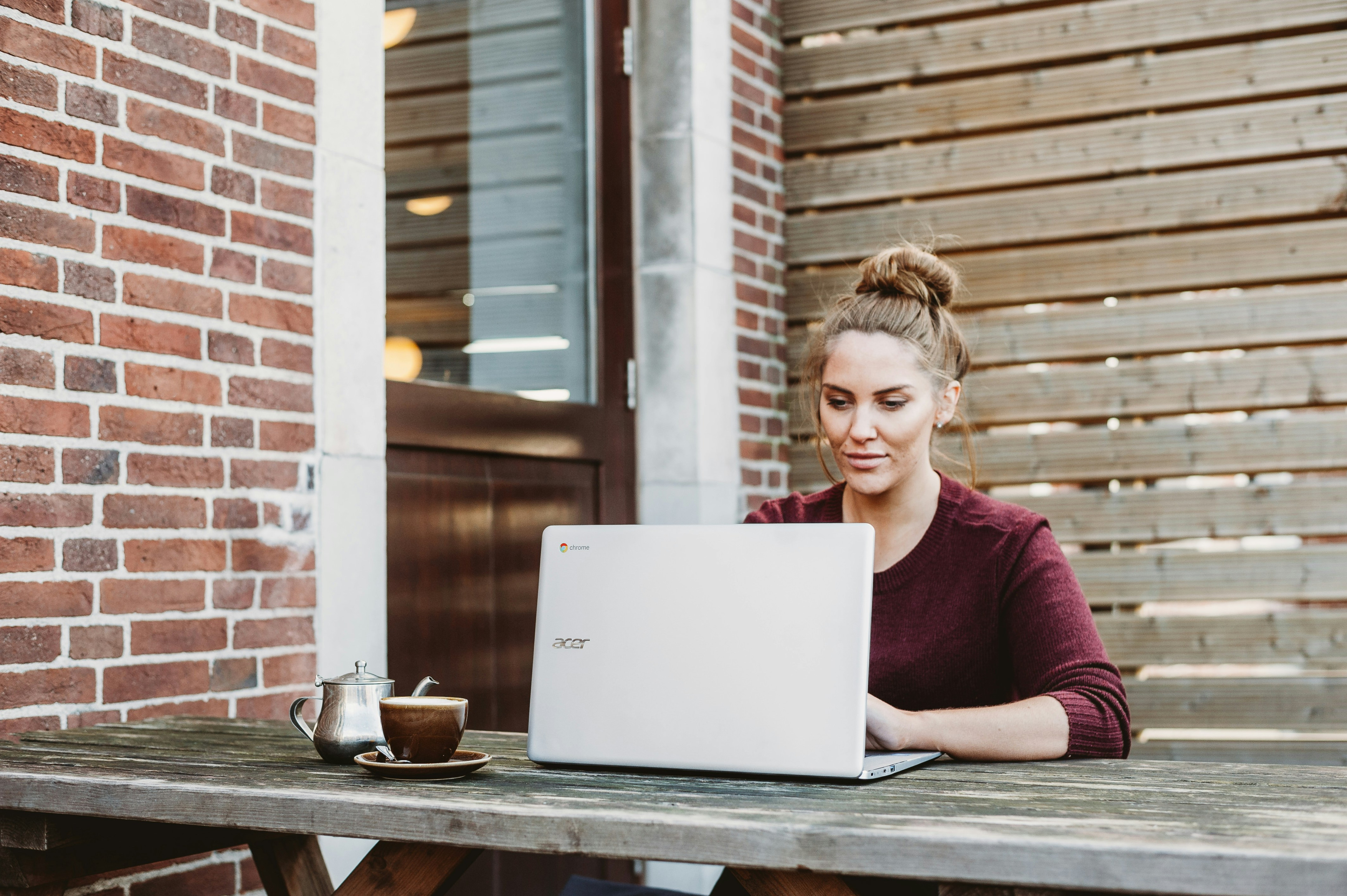 Person mit Laptop arbeitet draußen an einem Holztisch
