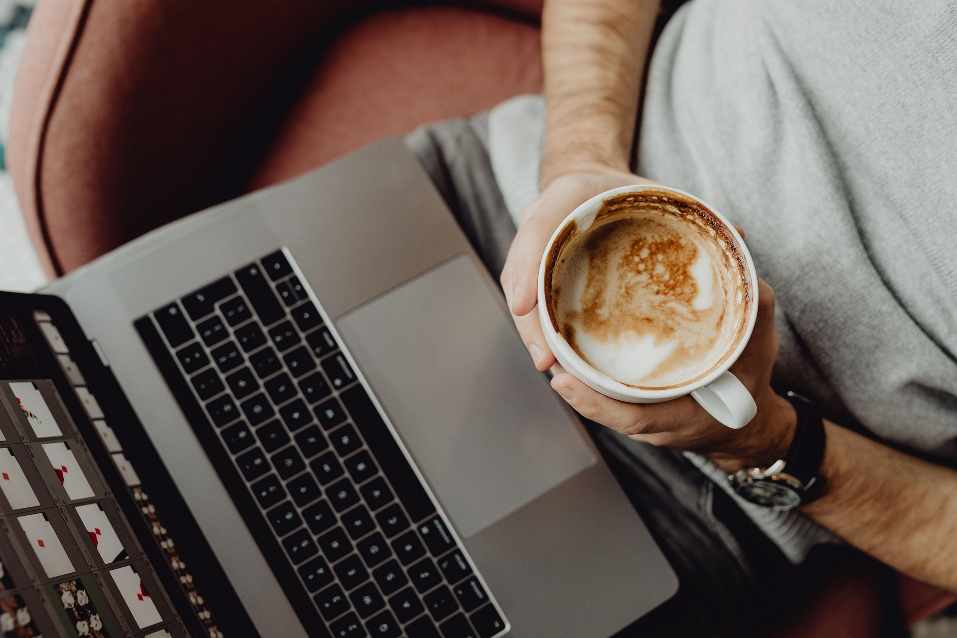 Laptop mit Person, die eine Tasse Kaffee hält