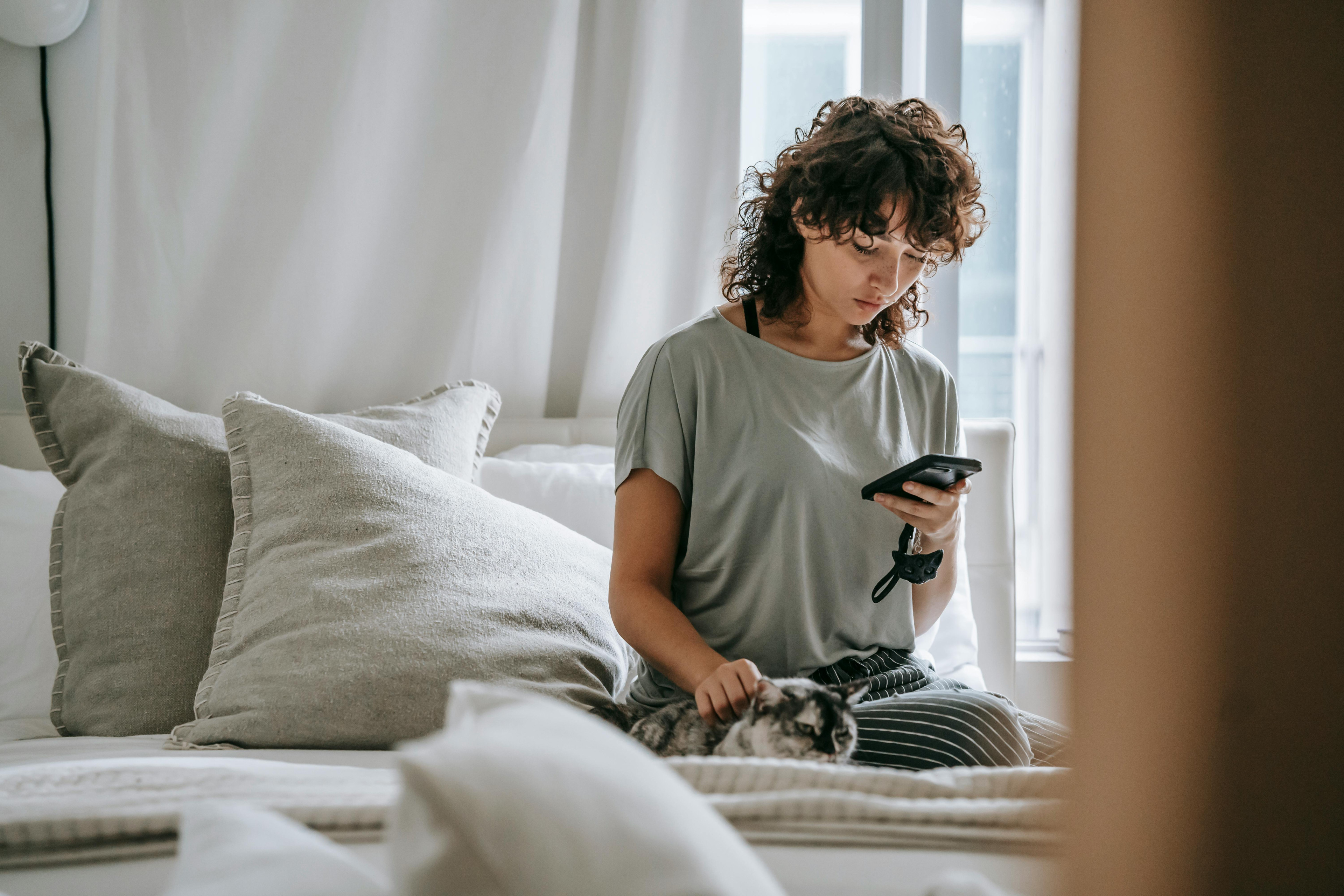 Person mit Katze und Smartphone auf dem Sofa