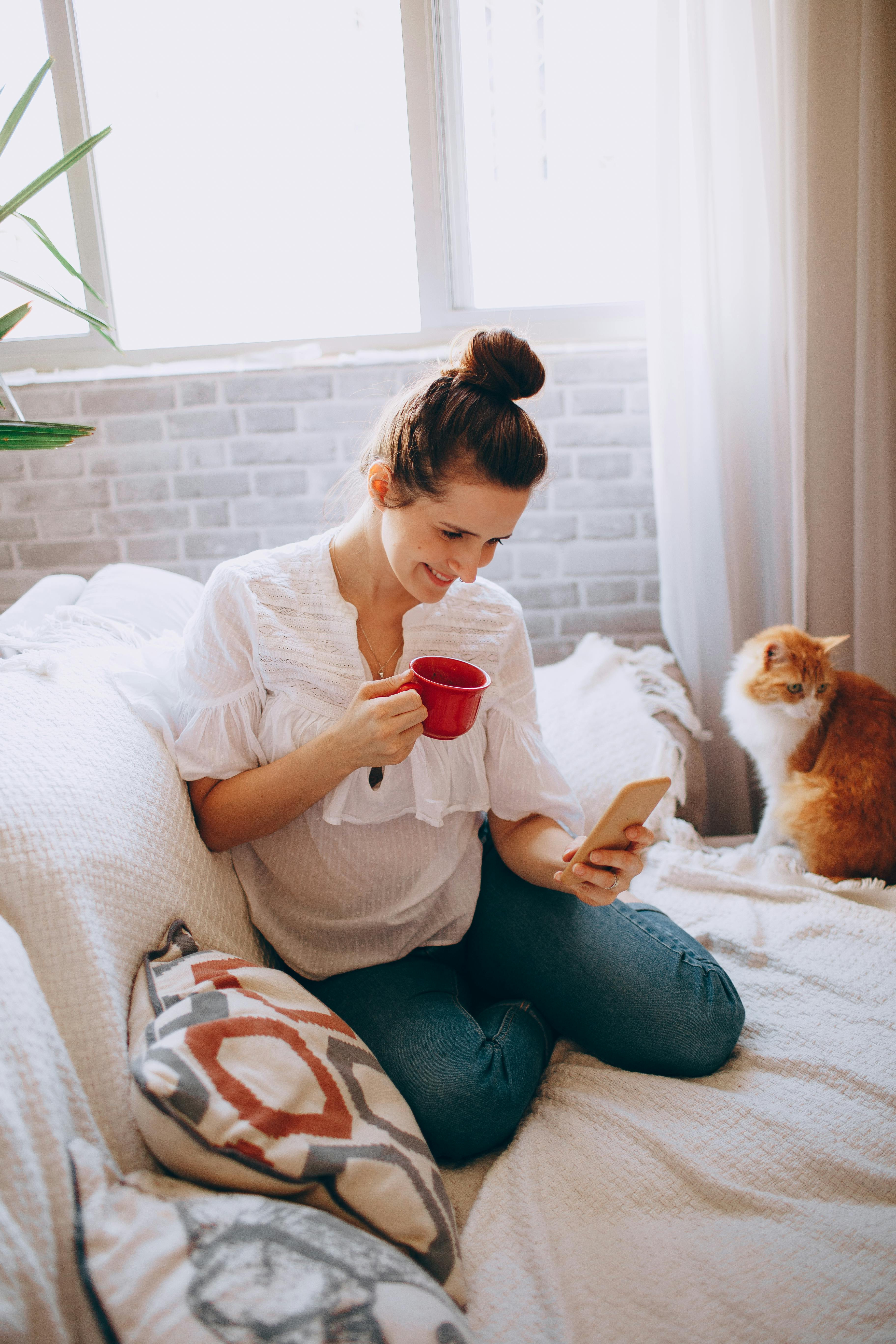 Person mit Smartphone und Katze auf dem Sofa, entspannt mit Kaffeetasse