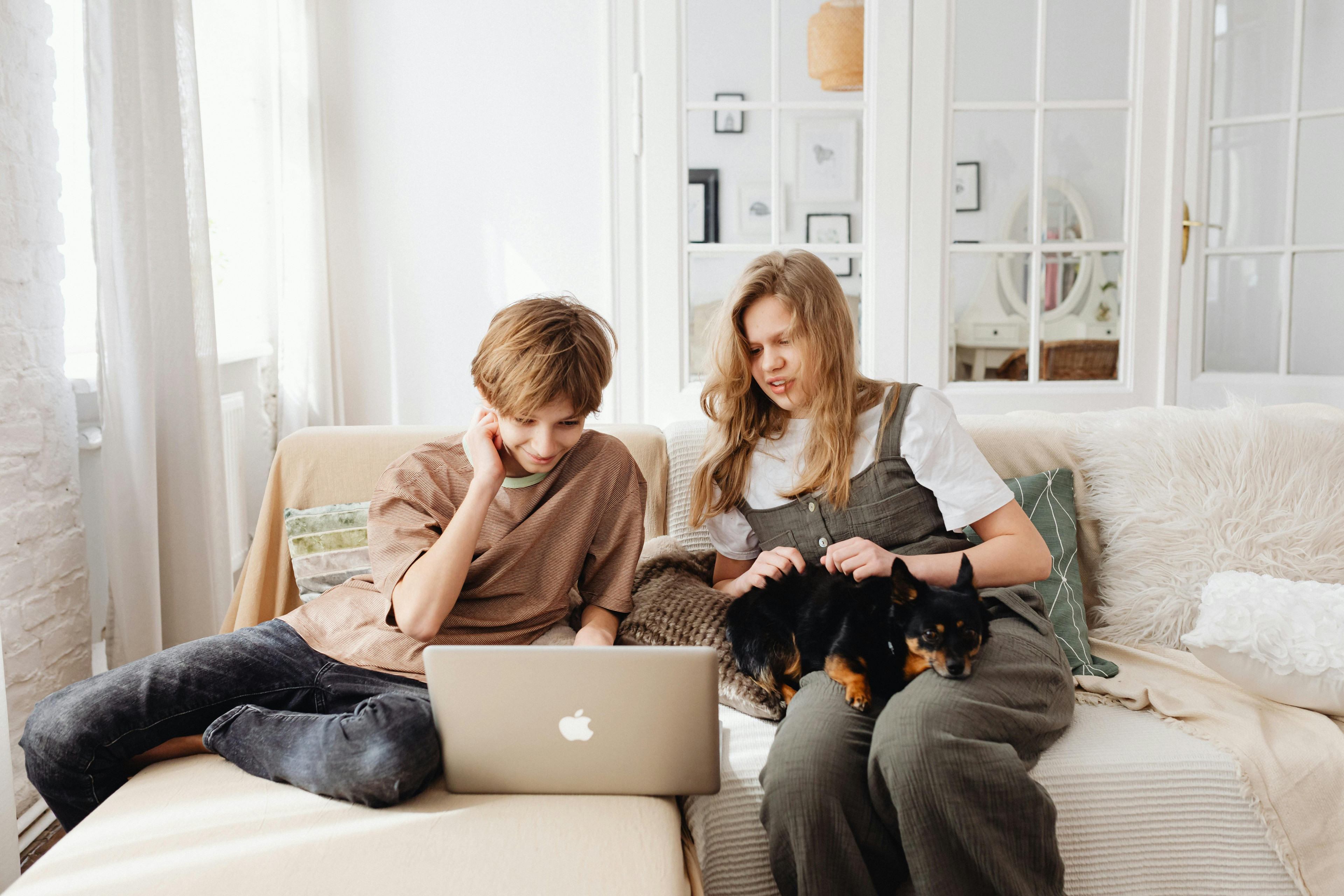Zwei Personen sitzen mit einem Haustier und einem Laptop auf dem Sofa
