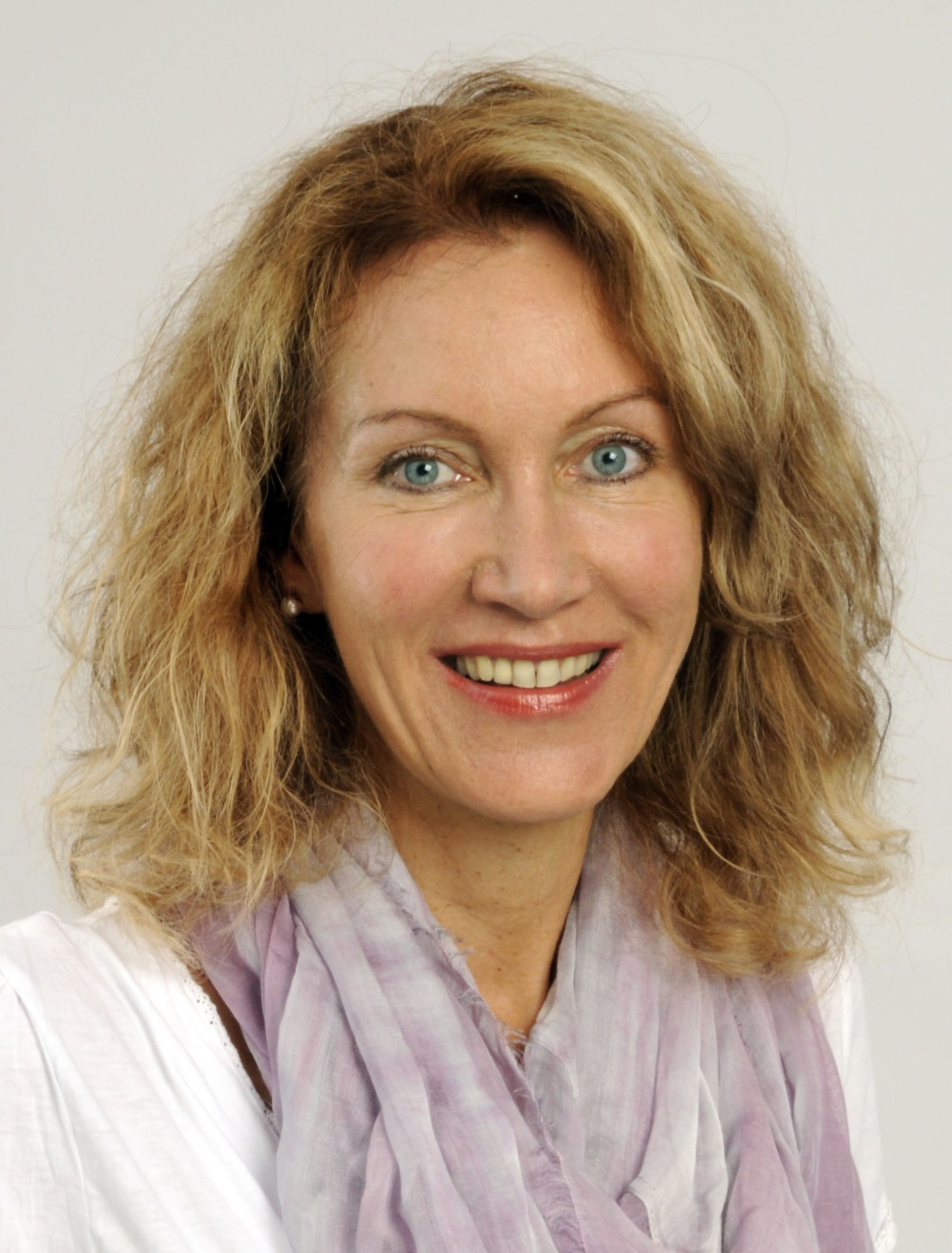 Portrait von Dr. med. Delia Grasberger, Ärztin mit blondem, lockigem Haar und lila Schal