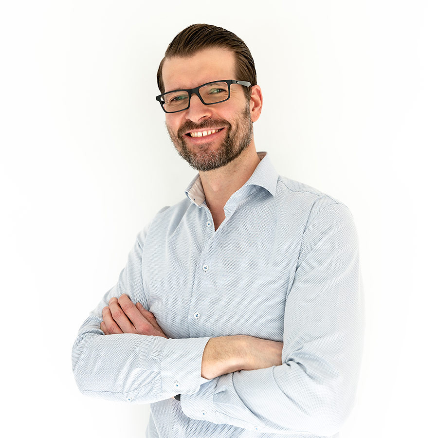 Portrait von Sven Bach mit verschränkten Armen vor weißem Hintergrund