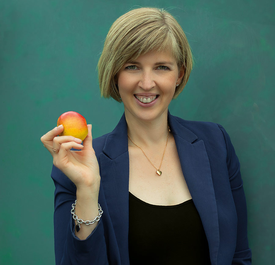 Julia Bierenfeld hält einen Apfel in der Hand, vor grünem Hintergrund, mit blauem Blazer