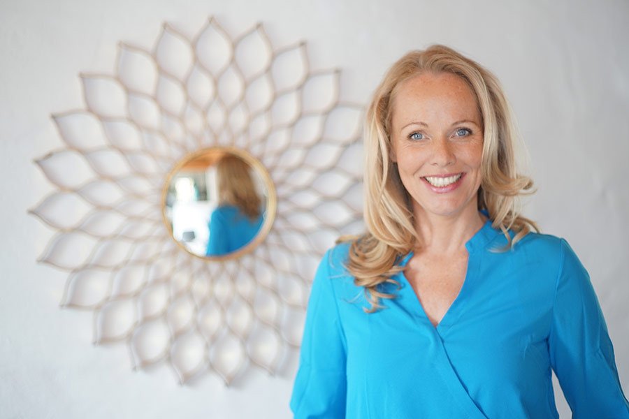 Katrin Bluege in blauer Bluse vor dekorativem Spiegel