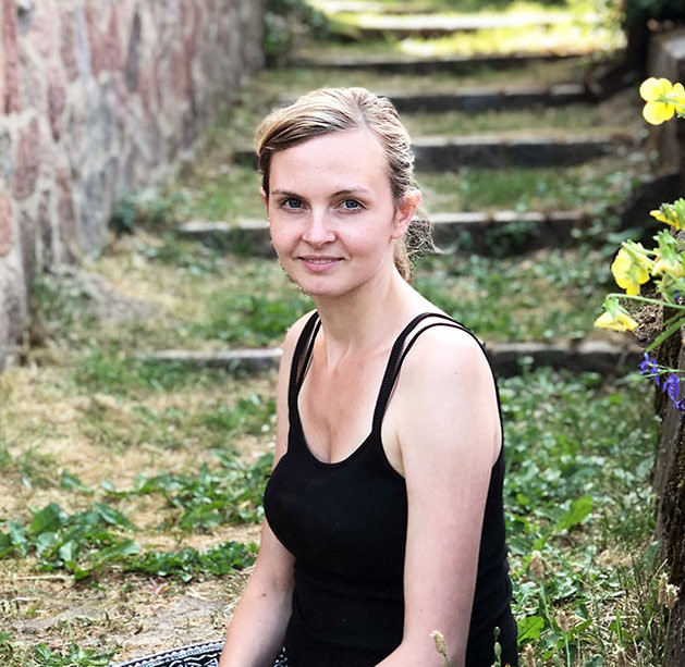 Nele Hillebrandt sitzt im Garten auf einer Steintreppe, umgeben von Blumen und Grünpflanzen