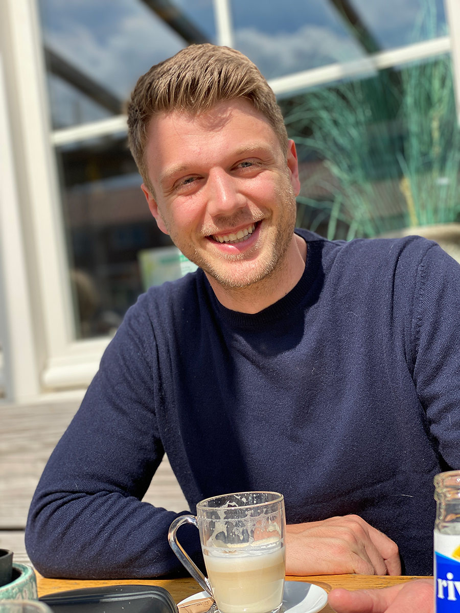 Kevin Hoffmann sitzt im Café und genießt ein Getränk bei Sonnenschein