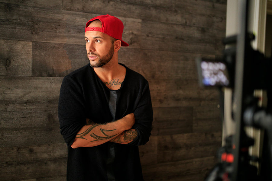 Benjamin Jaworskyj mit roter Kappe und Tattoos vor Holzwand