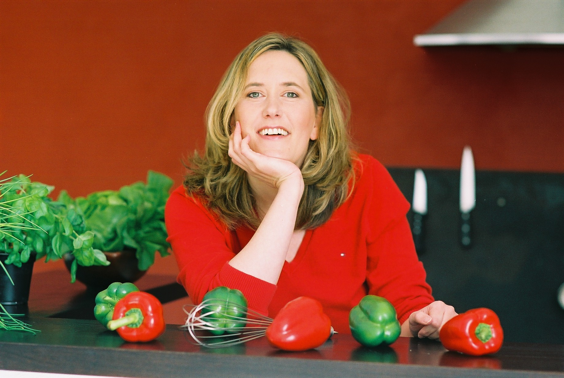 Marion Jetter in rotem Pullover in der Küche mit Paprika und Schneebesen