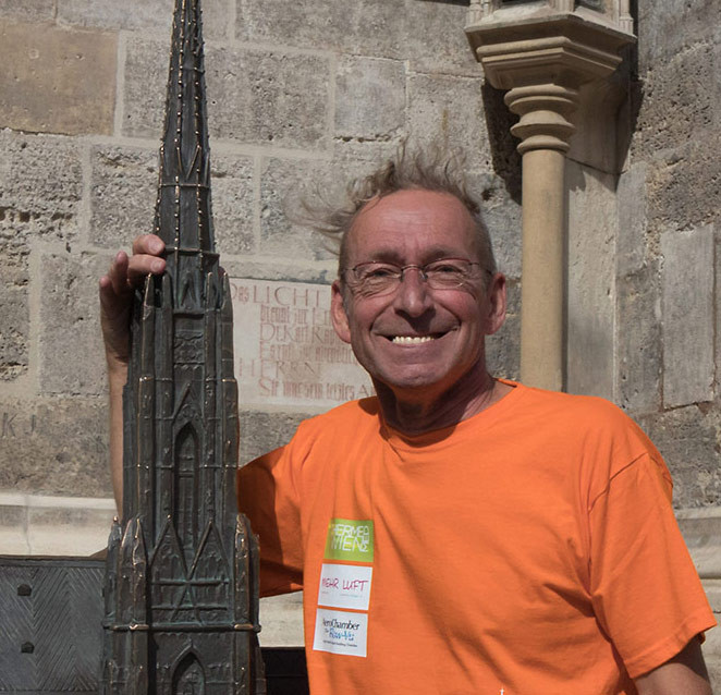 Jordan Eberhard steht neben einem Modell eines gotischen Kirchturms und trägt ein orangefarbenes T-Shirt.