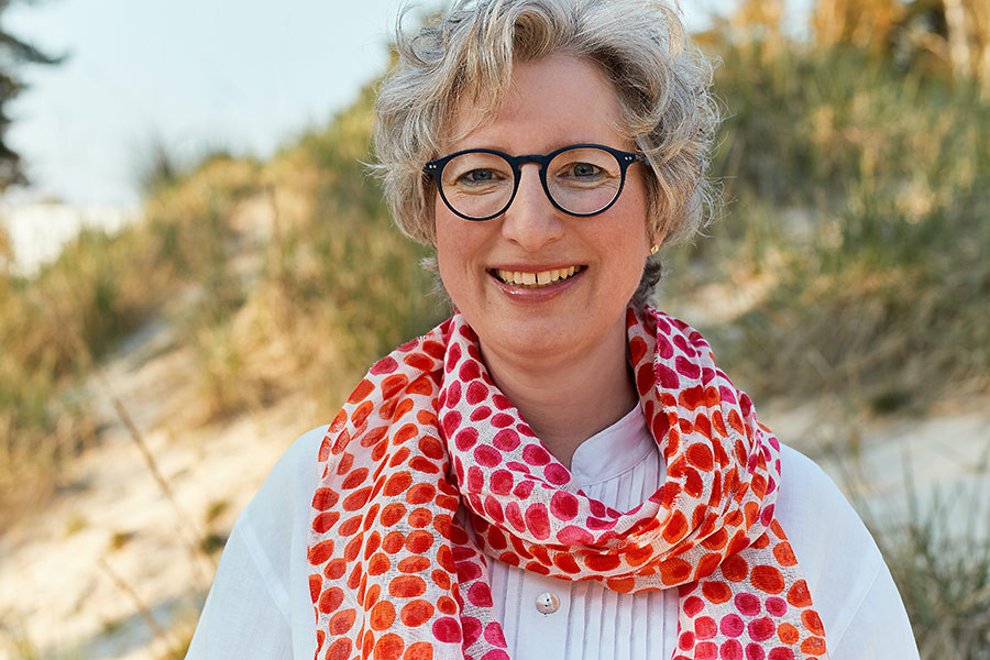 Portrait von Christine Kempkes mit weißer Bluse und rotem Schal im Freien