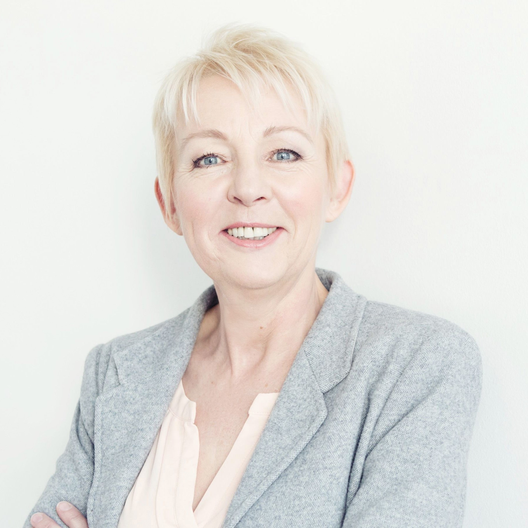Porträtfoto von Maria Lohmann im grauen Blazer vor hellem Hintergrund