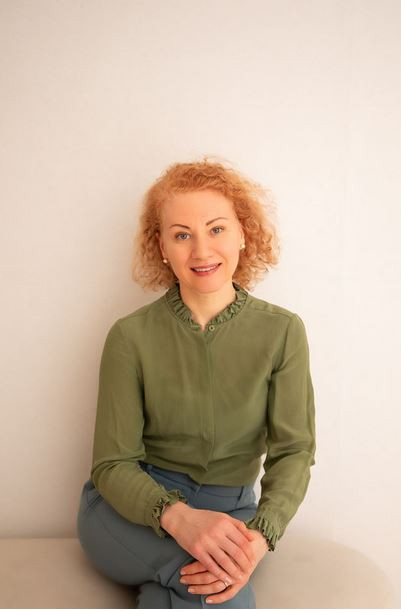 Porträtfoto von Dr. med. Anna Maier, Ärztin mit lockigem Haar und grüner Bluse