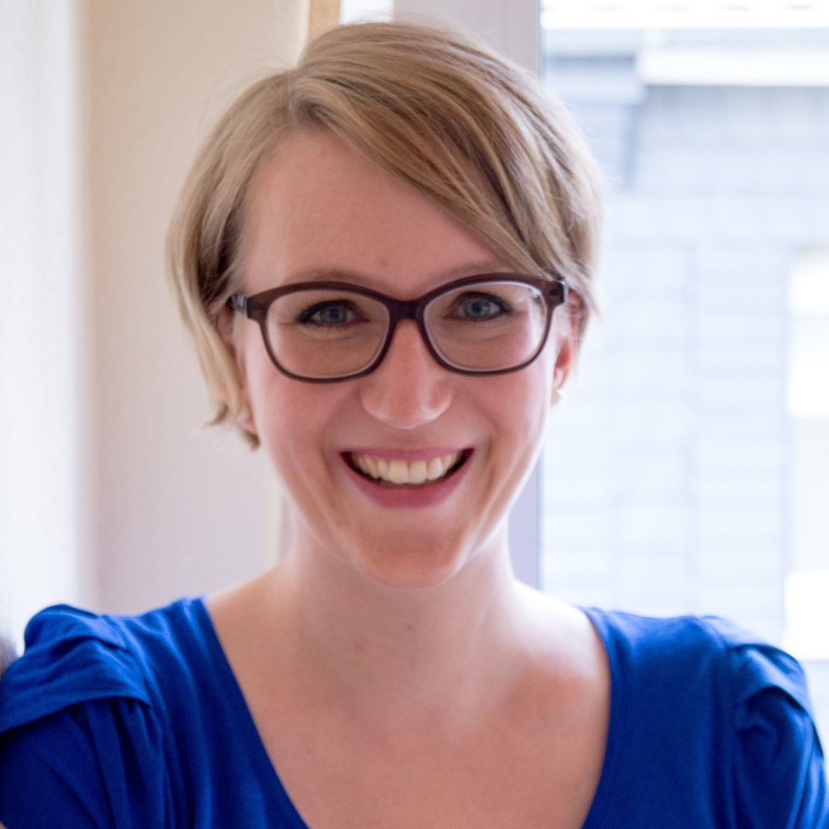 Porträt von Daniela Mainzer in einem blauen Oberteil am Fenster