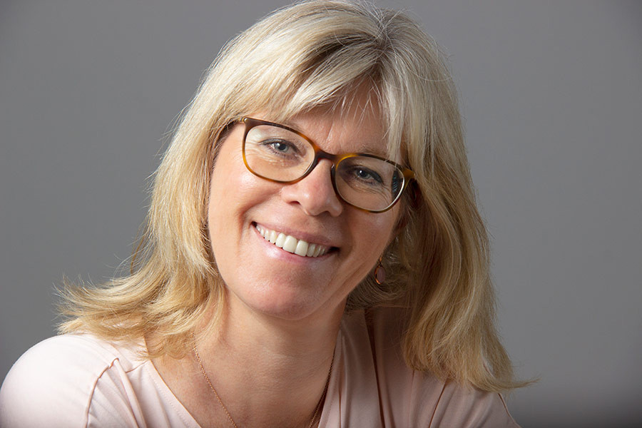 Portraitfoto von Ulla Nedebock mit blondem Haar vor grauem Hintergrund