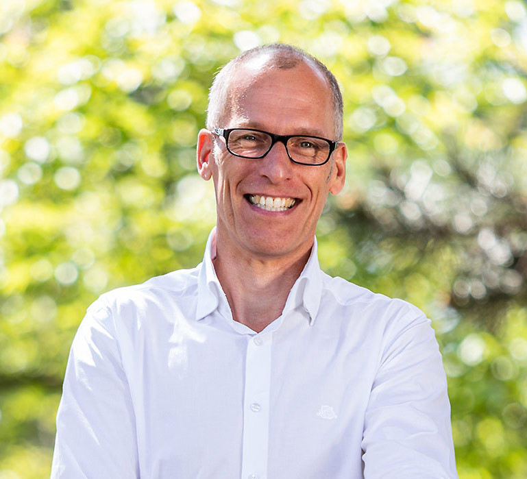 Porträt von Dr. Achim Pothmann im weißen Hemd vor grünem, natürlichem Hintergrund