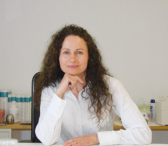 Beate Rinderer sitzt am Schreibtisch und trägt ein weißes Hemd