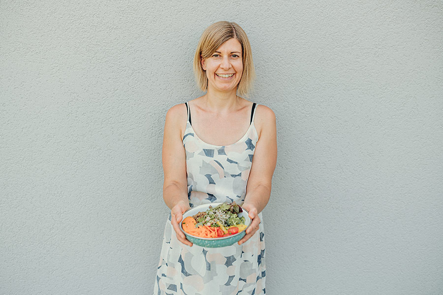 Moana Werschler hält eine bunte Bowl mit frischem Salat vor einer grauen Wand