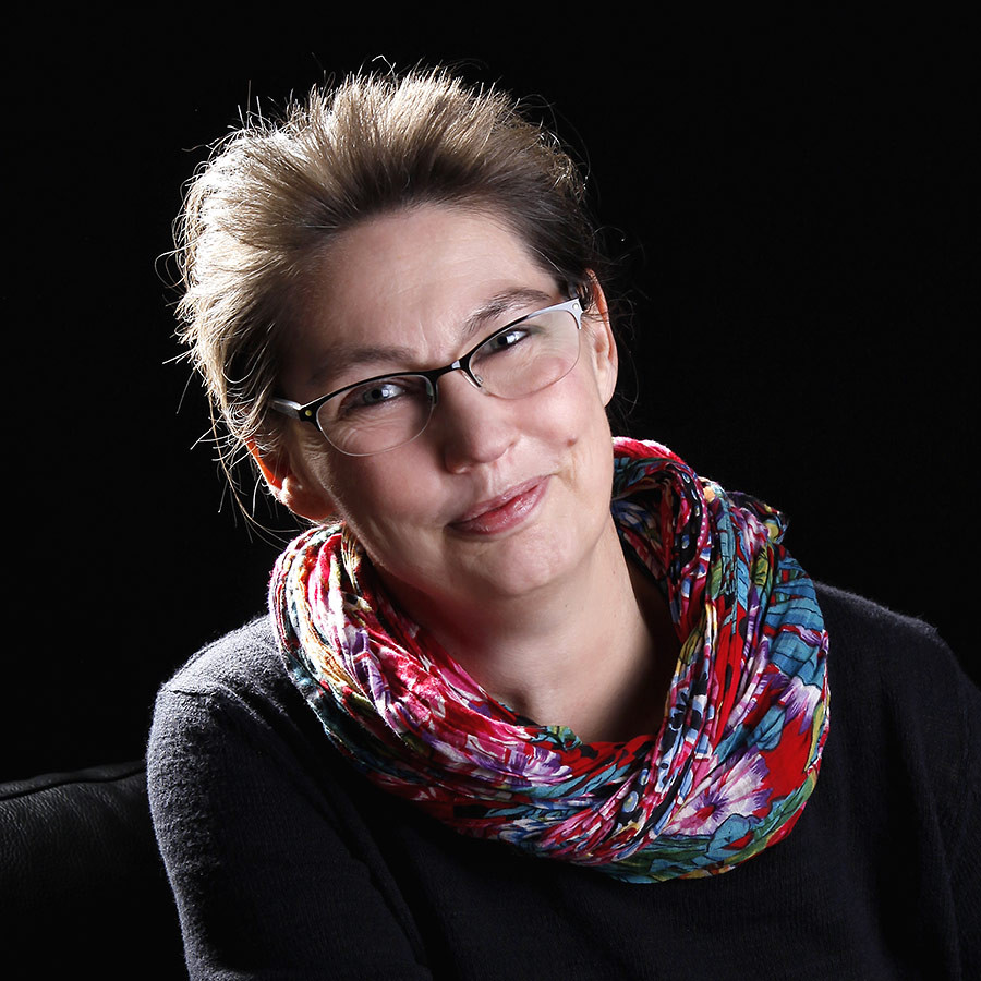 Porträtfoto von Iris Willecke mit buntem Schal vor schwarzem Hintergrund
