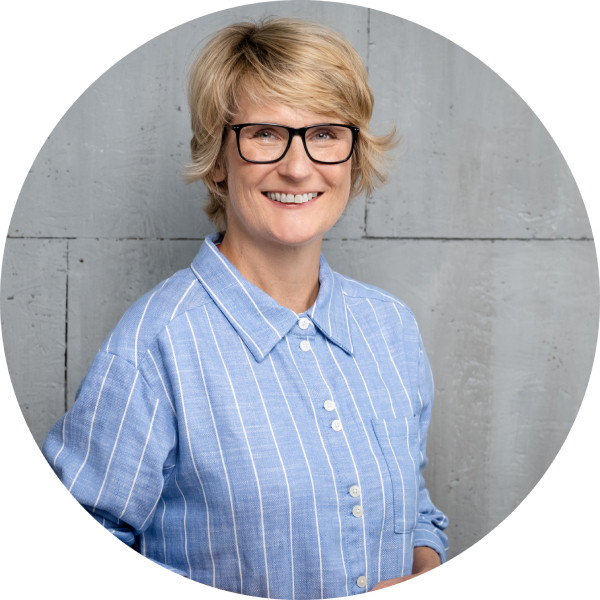 Portrait von Nicole Beck im Kreisformat, lächelnd mit Brille und blauer Bluse