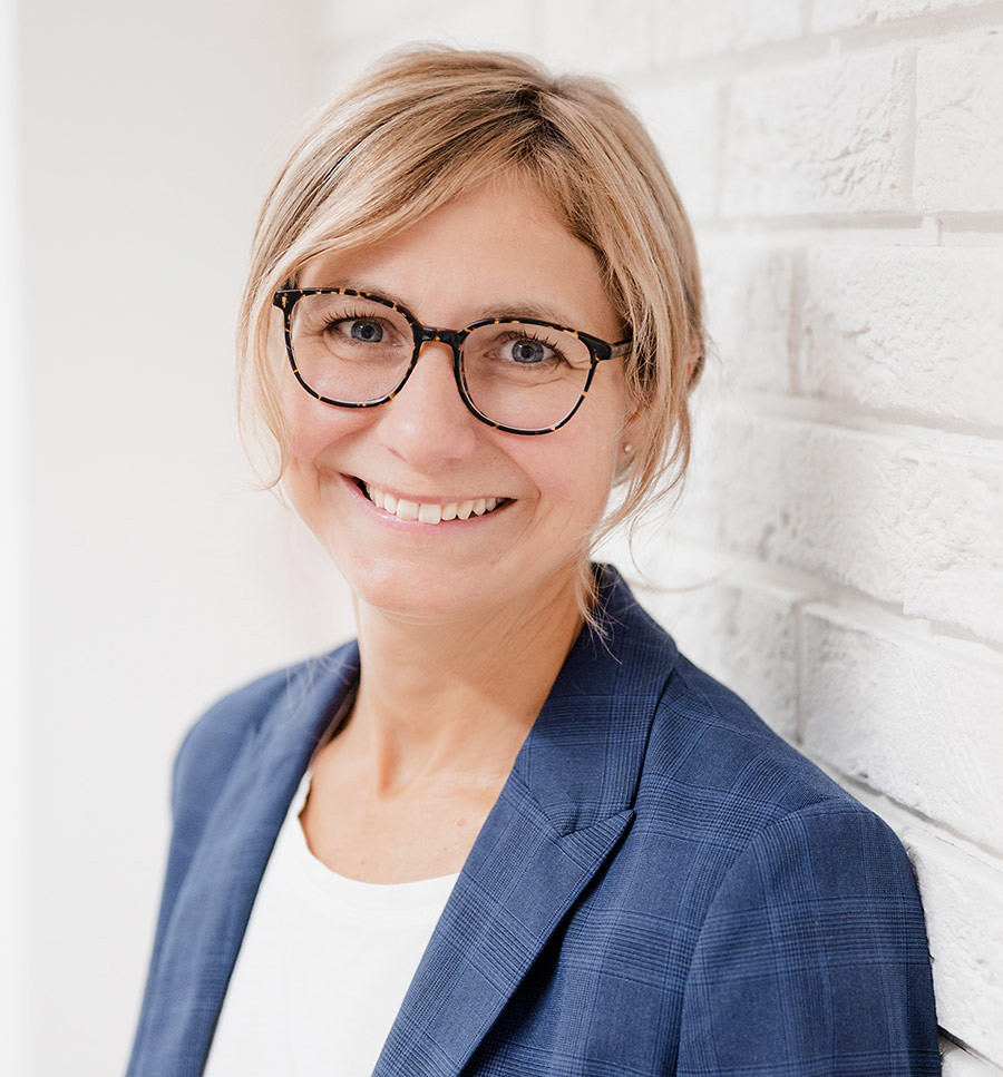 Michaela Veit-Wailzer lächelt freundlich, Porträtfoto vor weißer Wand