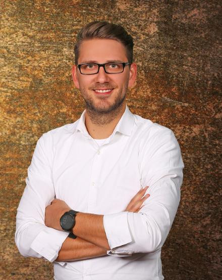 Portrait von Rick Lukas mit weißem Hemd vor braunem Hintergrund