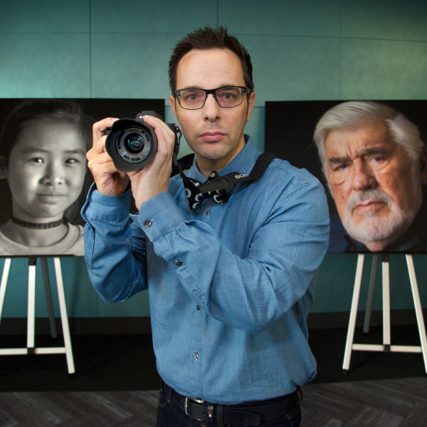 Fotograf Dirk Schiff mit Kamera vor Porträtfotos im Hintergrund