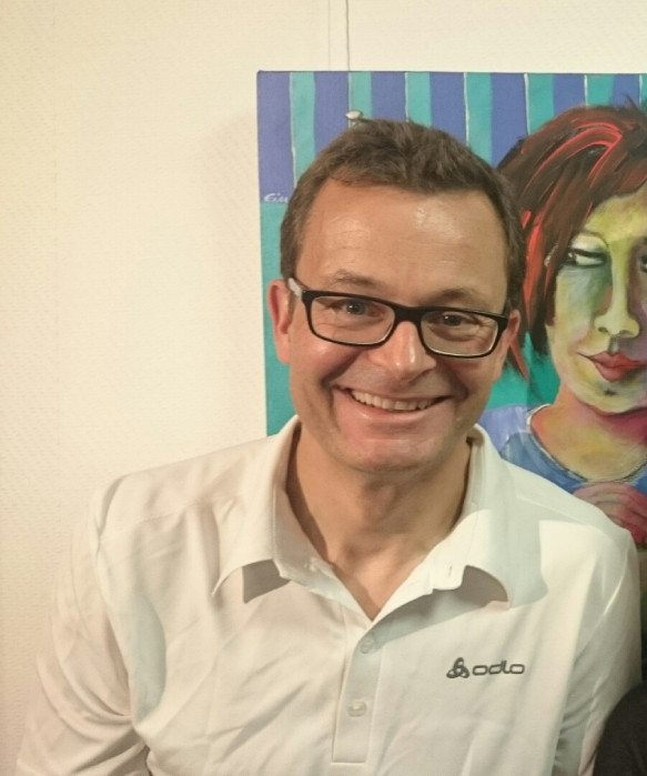 Dr. med. Florian Schuch lechelt vor einem bunten Gemlde, Portretfoto