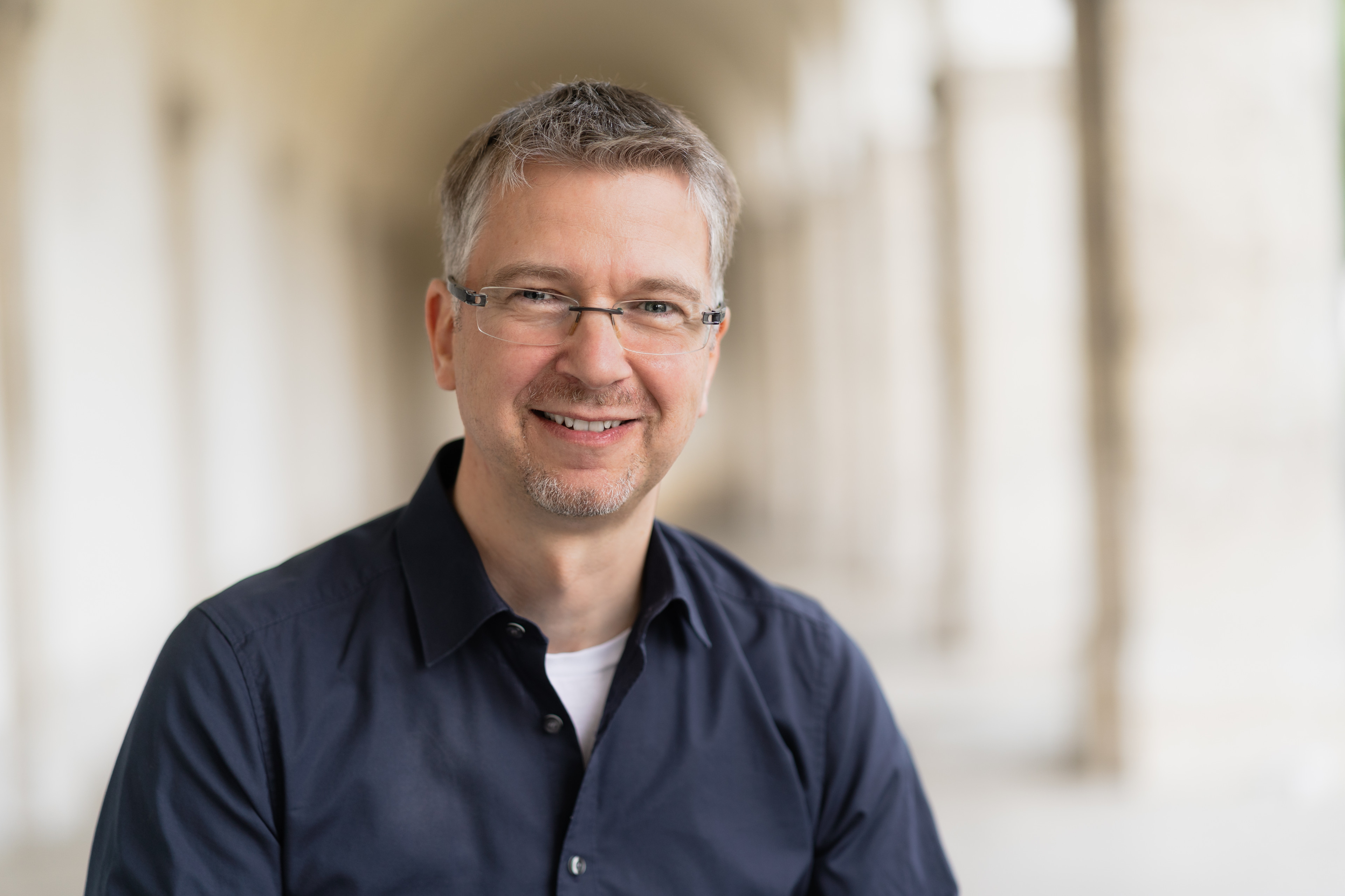 Portrait von Marco Weller, lächelnder Mann mit Brille im hellen Gang