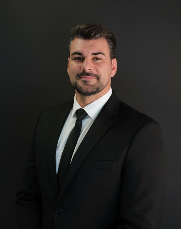 Geschäftsmann im schwarzen Anzug mit weißem Hemd und schwarzer Krawatte vor dunklem Hintergrund