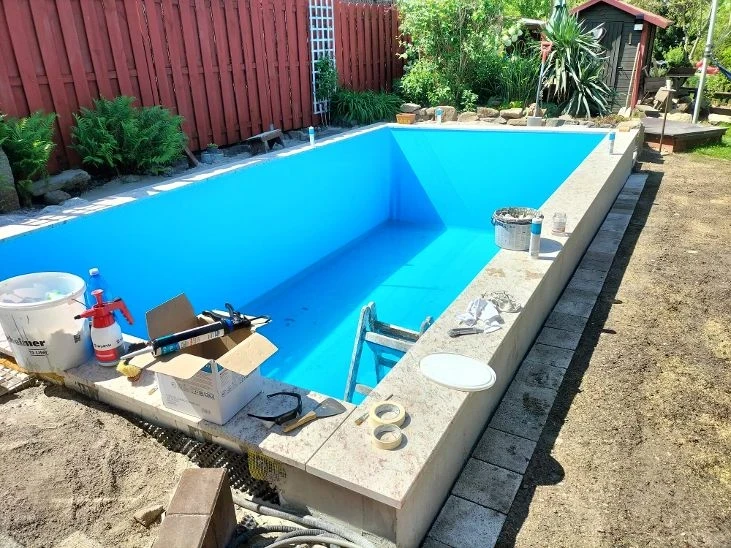 Poolumrandung aus Steinplatten bei einem rechteckigen Pool im Garten, Bauphase mit Werkzeugen und Baumaterialien