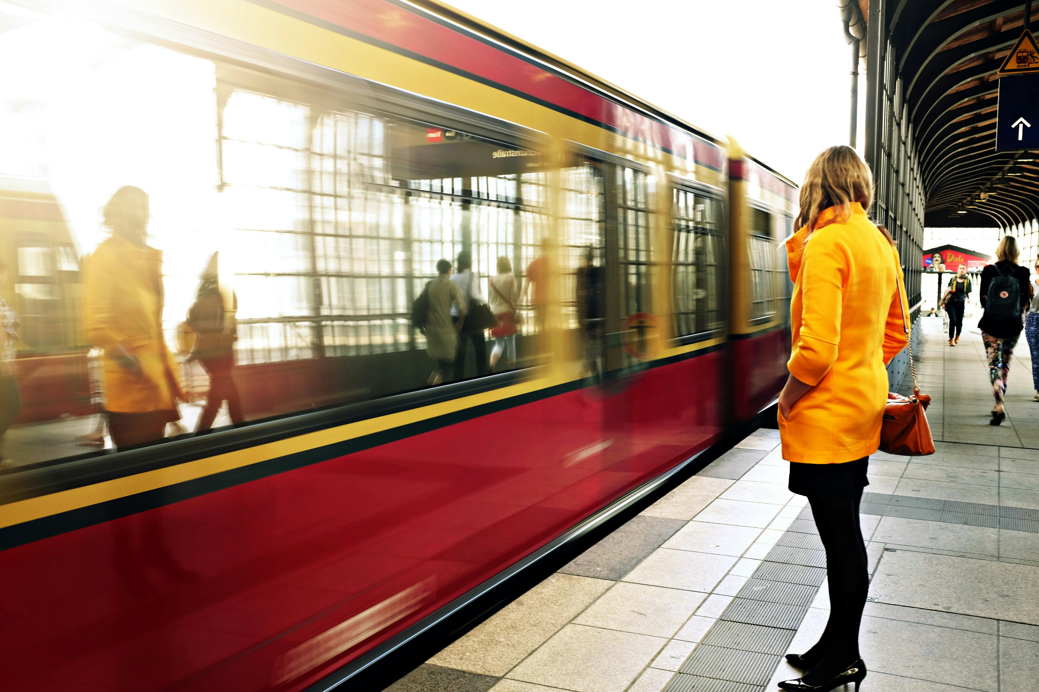 Person in einer gelben Jacke steht vor dem Zug mit dem Gesicht weg gedreht