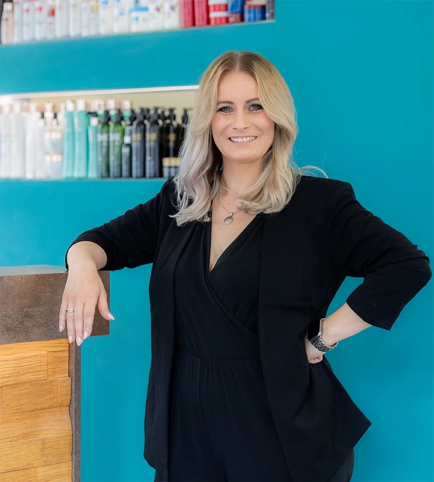 Friseurmeisterin Jane im Salon vor einem Regal mit Haarpflegeprodukten