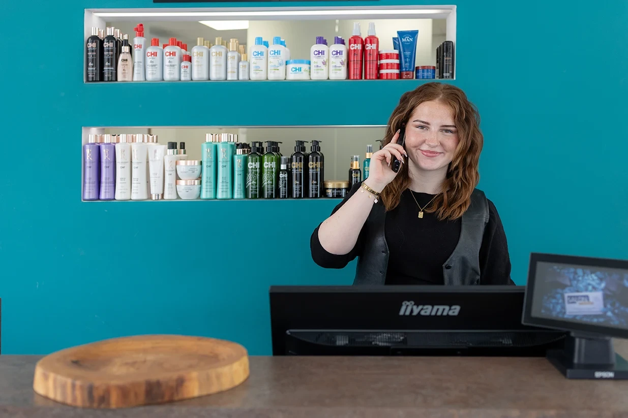 Empfangsbereich mit Zoe am Telefon und Friseurprodukten im Hintergrund