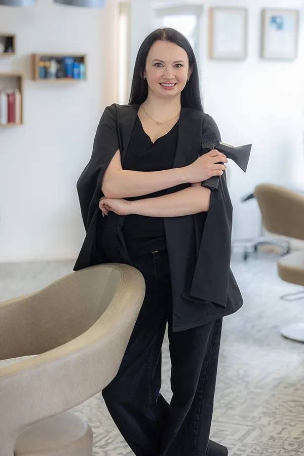 Alina als Friseurin im modernen Salon, steht lächelnd mit Föhn in der Hand