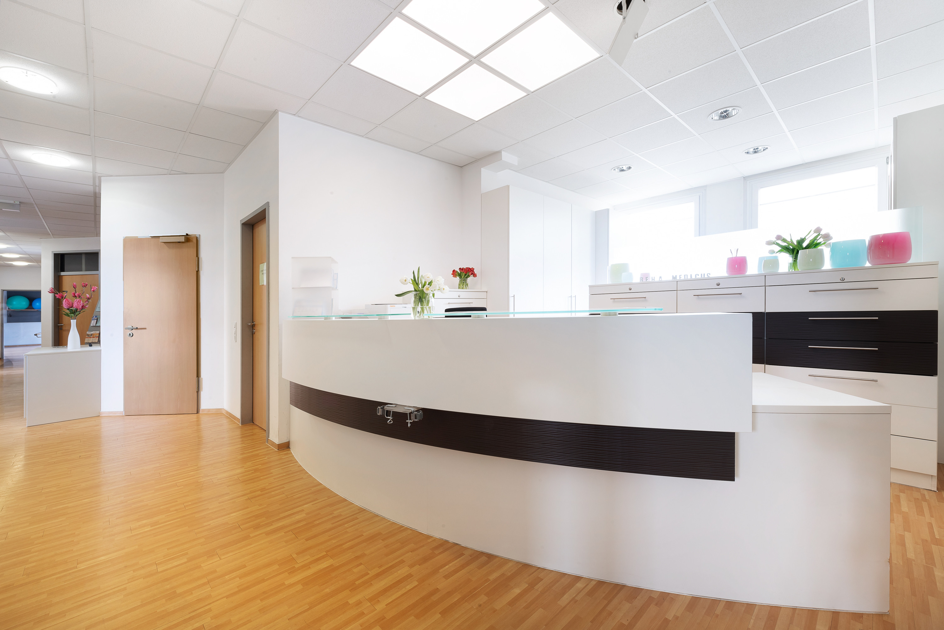 Moderner Empfangsbereich der Reha Medicus Praxis mit heller Einrichtung und Blumen auf dem Tresen