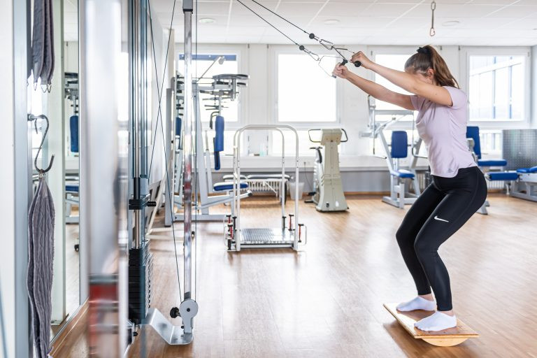 Frau trainiert an einem Reha-Seilzug in einer modernen Physiotherapie-Praxis