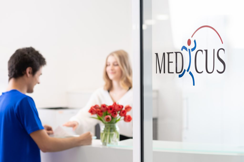 Empfangsbereich der Reha Medicus mit freundlicher Mitarbeiterin und Blumenstrauß am Tresen