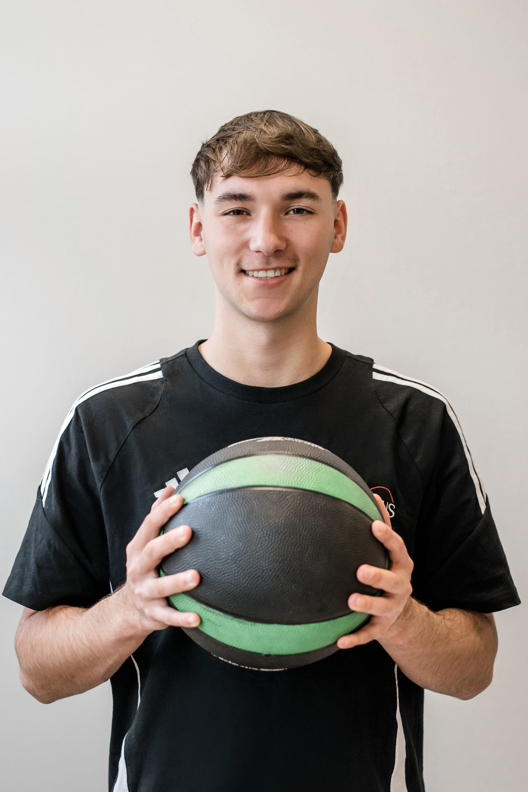 Jamie hält einen Basketball in den Händen, Sportler im schwarzen Trikot