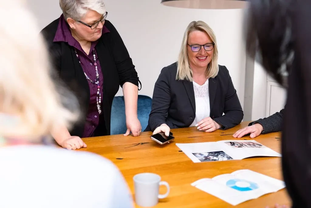 Großes Teammeeting mit mehreren Personen am Konferenztisch, Unterlagen und Smartphone