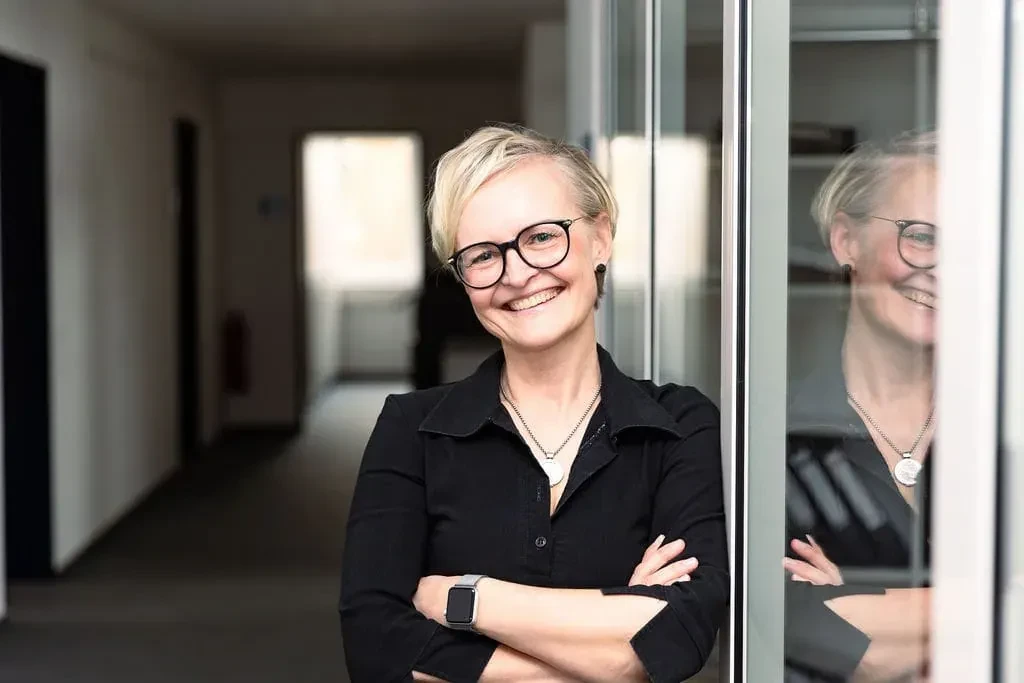 Porträt von Katrin Traut, lächelnd mit Brille und schwarzer Kleidung