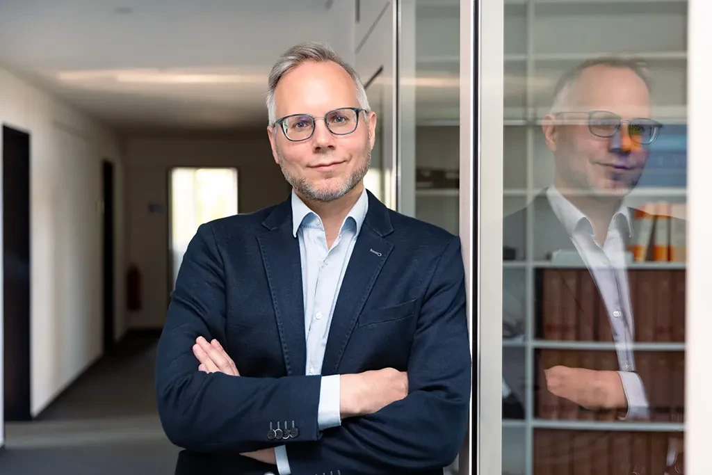 Michael Everlien steht mit verschränkten Armen im Büro und blickt selbstbewusst in die Kamera