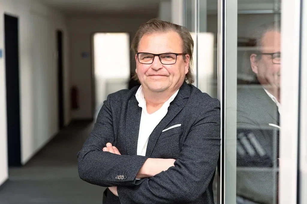 Porträt von Dr. Andreas Bierich mit Brille und Anzug, lächelnd und mit verschränkten Armen