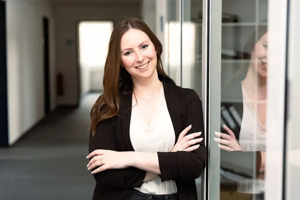 Portrait von Kim Cleve, lächelnde Frau im Business-Outfit vor Glaswand
